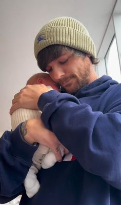 a man holding a baby in his arms and wearing a hat on top of him