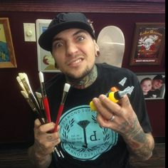 a man with tattoos holding up some paintbrushes and an object in his hand