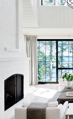 a living room filled with white furniture next to a fire place and large glass windows