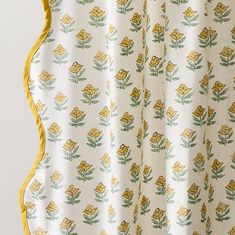 a white curtain with yellow flowers and green leaves on the bottom, hanging from a hook