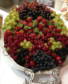 a platter filled with lots of different types of berries and grapes on top of a table