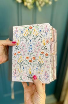 a woman holding up a small notebook with flowers on the front and back cover, in front of a blue door