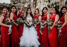 a group of women standing next to each other wearing red dresses and holding bouquets