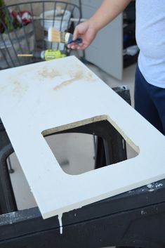 a person is painting the side of a table with white paint and a black brush