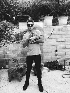 black and white photograph of a man holding a cat in his hands while standing next to a brick wall