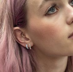 a woman with pink hair and piercings looks off to the side while wearing ear rings