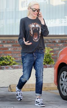 a woman walking down the street while talking on her cell phone and wearing ripped jeans