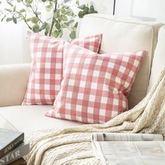 two red and white checkered pillows on a couch next to a coffee table with magazines