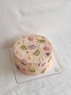 a pink cake with flowers on it sitting on top of a white tablecloth covered surface