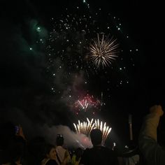 fireworks are lit up in the night sky with people taking pictures on their cell phones