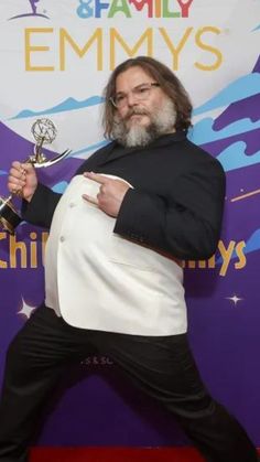 a man in a tuxedo poses with his award for outstanding performance at an event