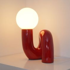 a red lamp sitting on top of a white shelf next to a light bulb in the shape of a letter