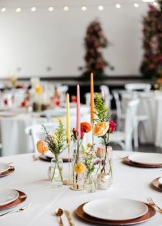 the table is set with candles and flowers in glass vases on top of plates