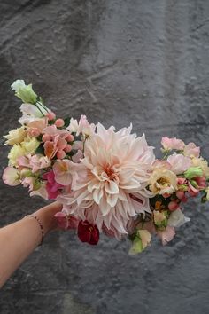 a hand holding a bouquet of flowers in front of a stone wall with water droplets on it