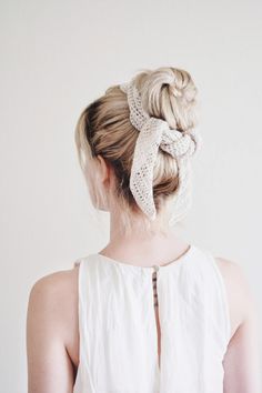 a woman wearing a white top with a knotted hair tie in her back, looking off to the side