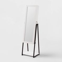 a white and black standing mirror on top of a wooden stand next to a wall