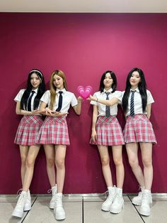 three girls in school uniforms standing next to a pink wall and one girl is holding a heart shaped balloon