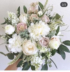 a bouquet of white and pink flowers in someone's hand with green leaves on it