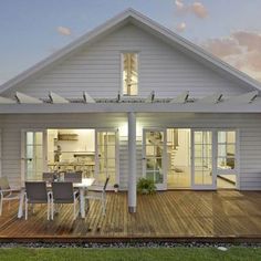 a white house with wooden decking and patio furniture at dusk, in the evening