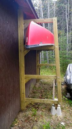 a red canoe sitting on top of a wooden stand next to a building in the woods