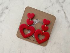 two red heart shaped earrings sitting on top of a card with the word love written in it