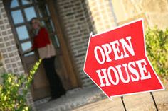 a red open house sign sitting in front of a doorway with a woman standing outside