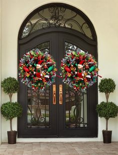 two christmas wreaths sitting on the front door of a house with potted trees