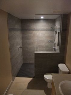 a bathroom with a walk in shower next to a white toilet and sink under a window