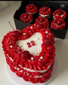 a heart shaped cake sitting on top of a white plate next to cupcakes