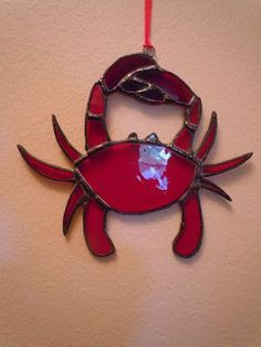 a red glass crab ornament hanging on a wall next to a white wall