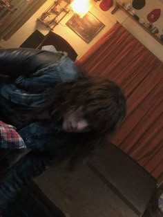 a man with long hair sitting on top of a wooden table next to a window