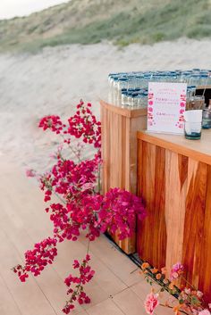 the flowers are blooming next to the wooden counter at the beachside bar with water bottles on it