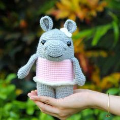 a hand holding a small gray crocheted stuffed animal with a pink dress on it's chest