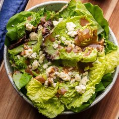 a bowl filled with lettuce and cheese on top of a wooden table