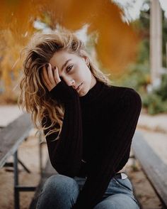 a woman sitting on top of a wooden bench next to a park bench and holding her hand near her face