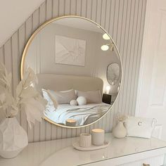 a bedroom with a round mirror on the wall and a white dresser in front of it