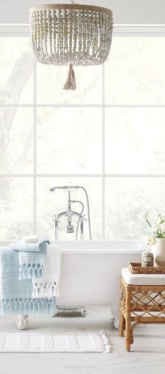 a white bath tub sitting under a chandelier next to a table with flowers