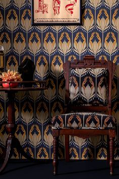 a wooden chair sitting next to a table with a vase on it and a painting above it