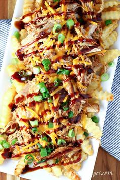 a white plate topped with cheesy potatoes covered in bbq sauce and green onions