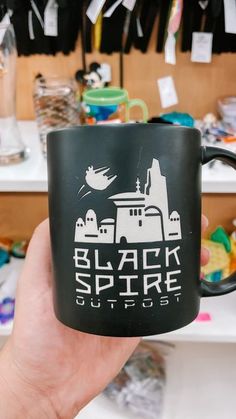 a hand holding a black coffee mug with the words black spire outdoors printed on it