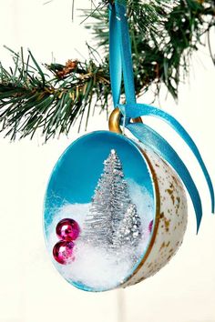 a christmas ornament hanging from a tree branch with snow and trees on it