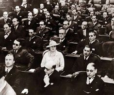 an old black and white photo of people sitting in rows with hats on their heads