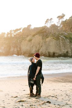 a man and woman standing on top of a sandy beach