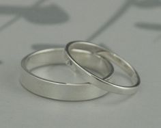 two silver wedding rings sitting on top of a white table next to a shadow of flowers