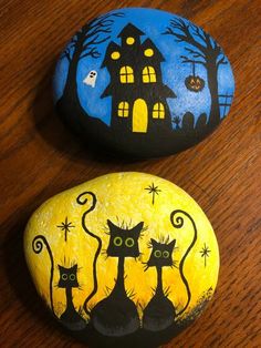 two painted rocks with cats on them and a house in the background, one is yellow and the other is black