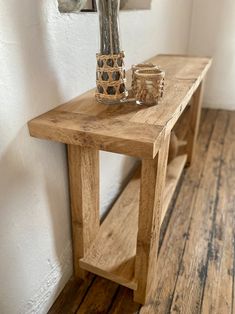 a wooden table with a vase and candle holder on it next to a white wall