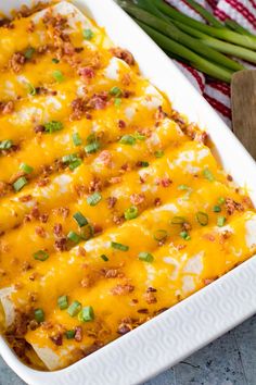 an enchilada casserole in a white dish with green onions on the side