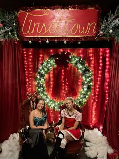 two women sitting on chairs in front of a christmas display