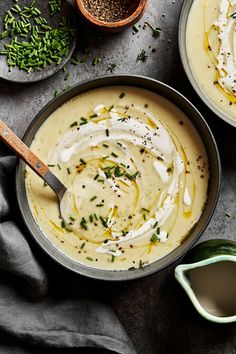 two bowls filled with cream and herbs on top of a gray tablecloth next to small dishes