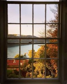 an open window looking out onto the water and trees in front of it with fall foliage